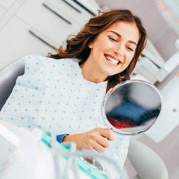 happy woman examining her teeth in a mirror at the dentist's office