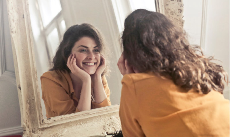 girl leaning her chin in her hands smiling into the mirror admiring her white teeth